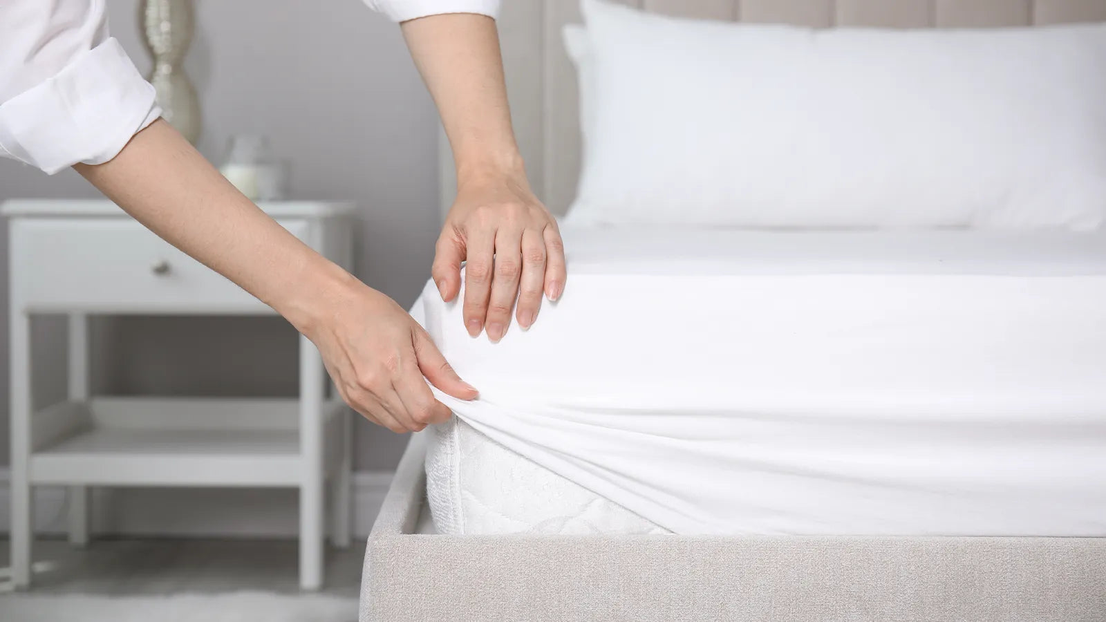 A person fitting a fitted sheet on a bed